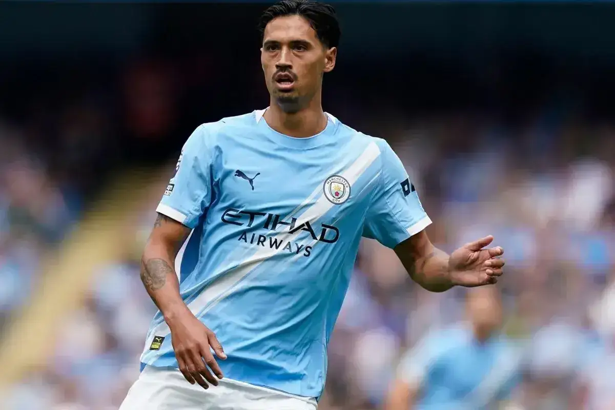 Piłkarz Man City w błękitnej koszulce z białymi pasami, z logo klubu i sponsora. Jeden z wielu zawodników tej drużyny.