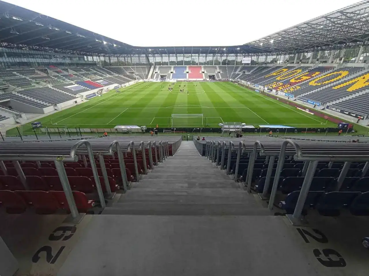 Puste trybuny stadionu Pogoni, sektor gości. Piłkarze na murawie, gotowi do gry.