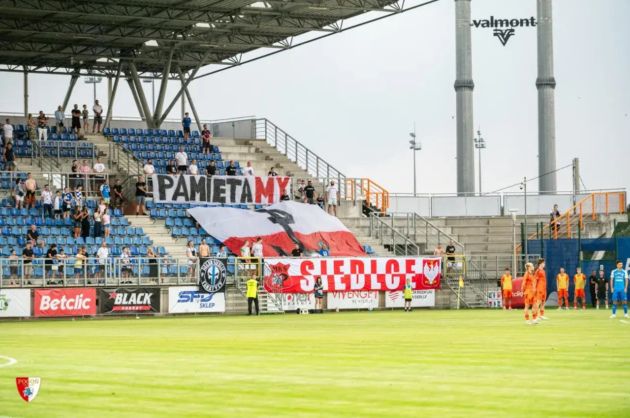 Trybuna stadionu Pogoń Siedlce z kibicami i transparentami.