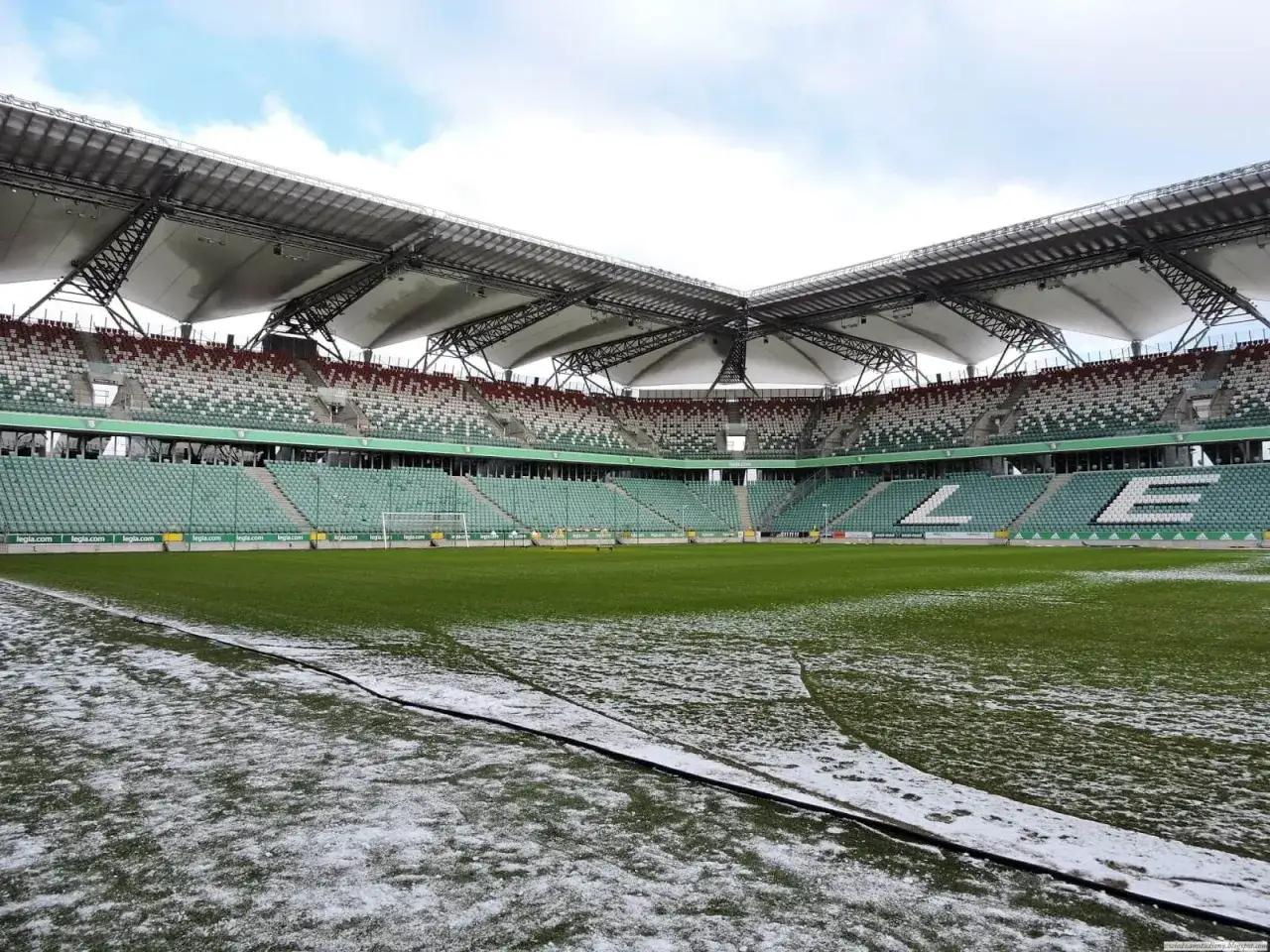 Pusta trybuna stadionu Wojska Polskiego z zieloną murawą i resztkami śniegu.