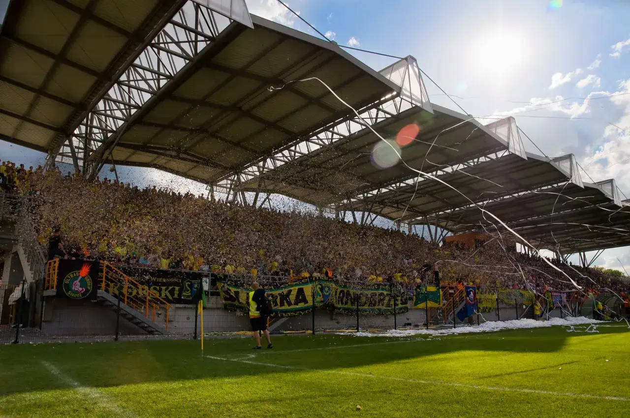 Tłum kibiców Siarki Tarnobrzeg na stadionie, sypiący się konfetti i wstążki.