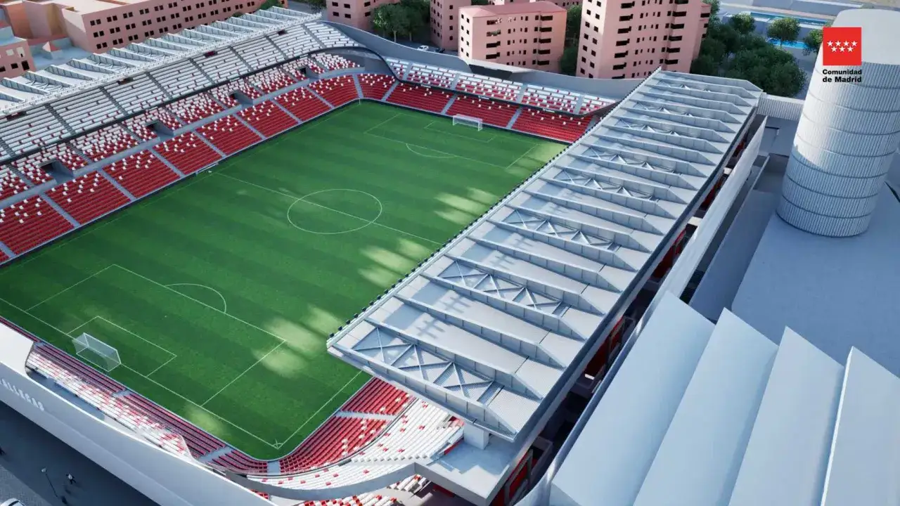 Nowoczesny stadion Rayo Vallecano z zieloną murawą i czerwono-białymi trybunami, otoczony budynkami.