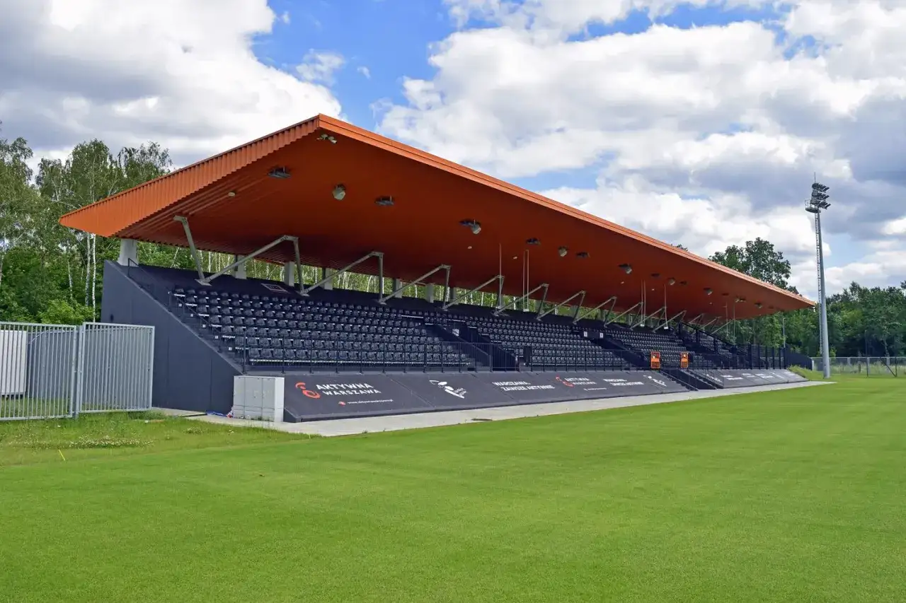 Nowoczesny stadion Hutnik Warszawa z pomarańczowym zadaszeniem i rzędami czarnych siedzeń.