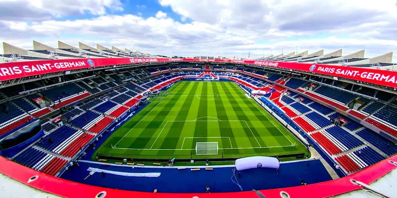 Pusta trybuna stadionu Parc des Princes, z czerwono-niebieskimi siedzeniami i zieloną murawą, gotowa na mecz Paris Saint-Germain.