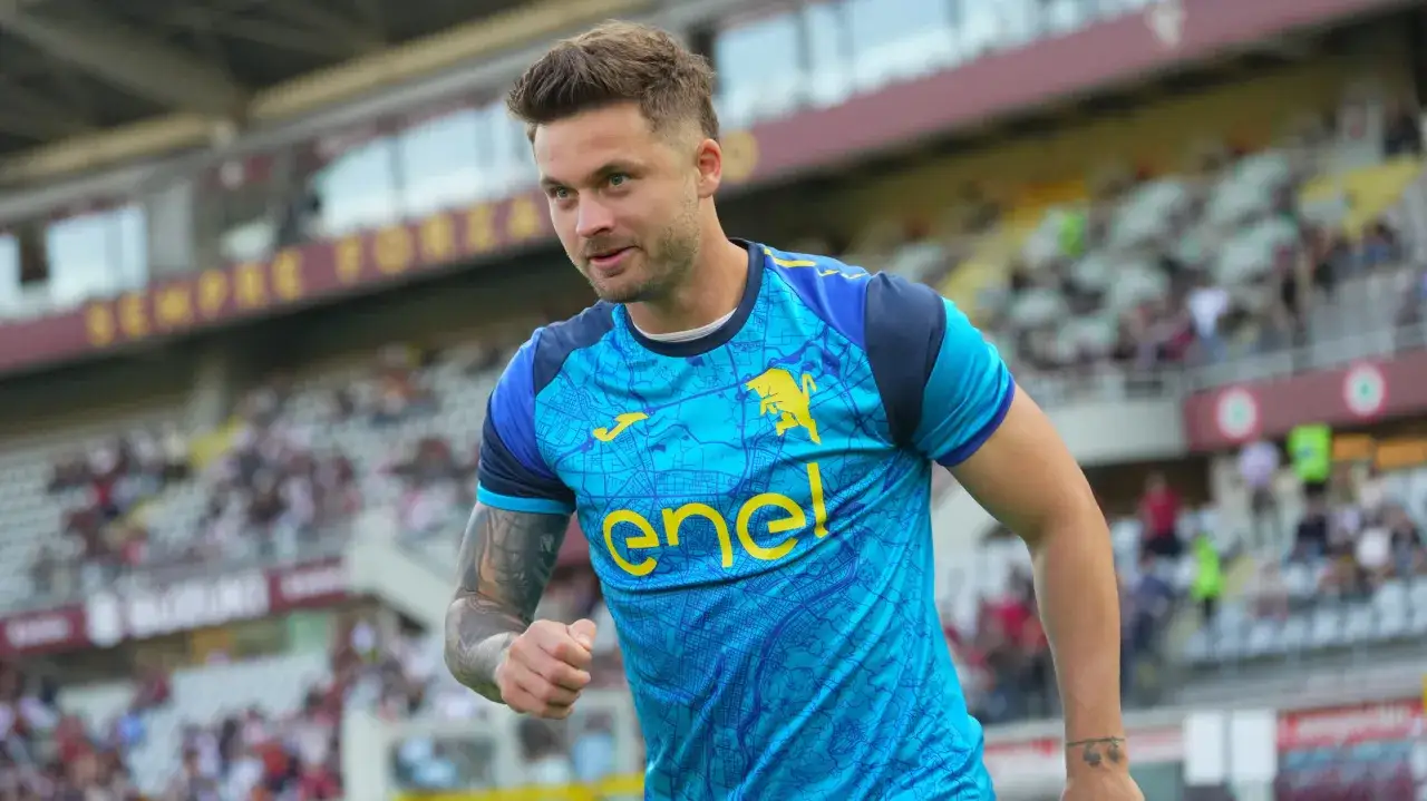 Piłkarz w niebieskiej koszulce z żółtym logo, kiedy gra Linetty, na tle trybun stadionu.