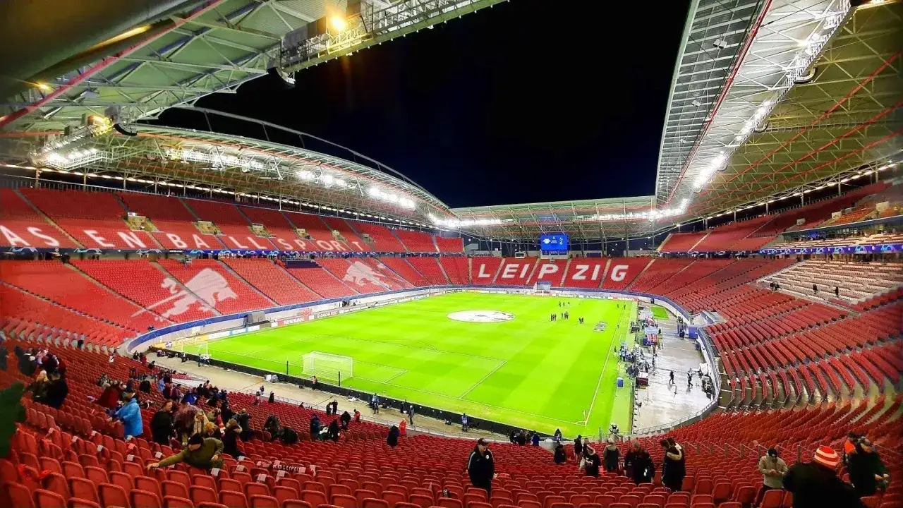 Pusta trybuna na Red Bull Arena Leipzig, z czerwonymi siedzeniami i zieloną murawą.