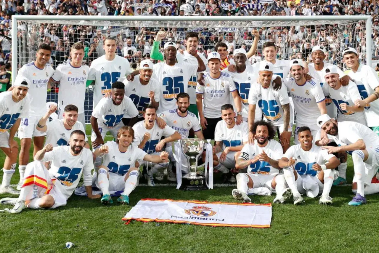 Drużyna Real Madryt 2017 świętuje zwycięstwo z pucharem. Piłkarze w białych strojach pozują do zdjęcia na tle bramki i trybun.