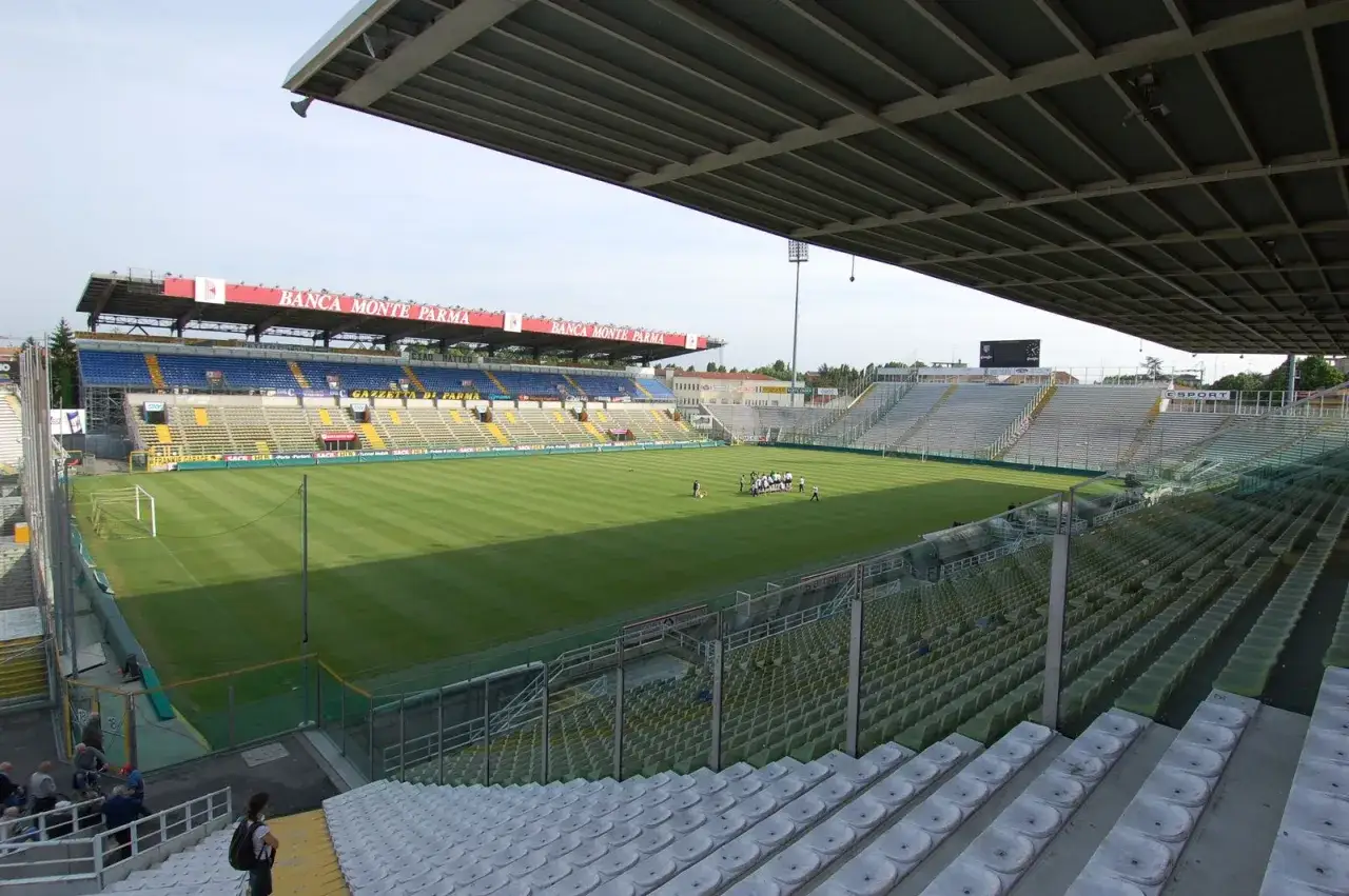 Stadion piłkarski z murawą, trybunami i kilkoma zawodnikami na boisku. To dom drużyny Parma Calcio 1913.