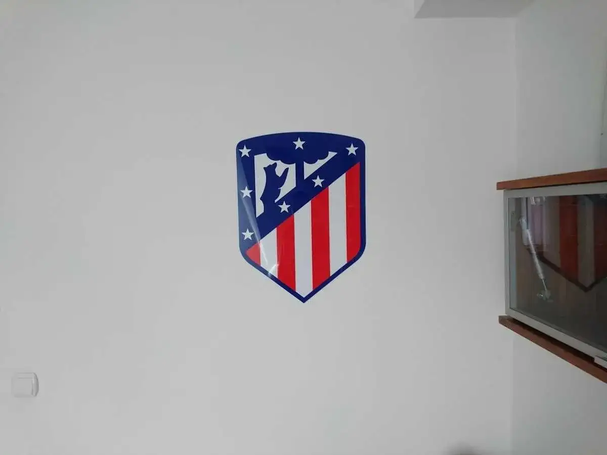 Logo Atletico Madryt na białej ścianie. Dumnie prezentuje się godło klubu z niedźwiedziem i drzewem.