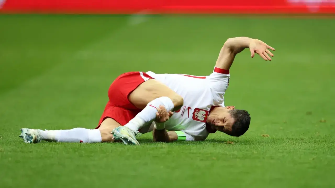 Robert Lewandowski, grający na pozycji napastnika, leży na boisku, trzymając się za nogę.