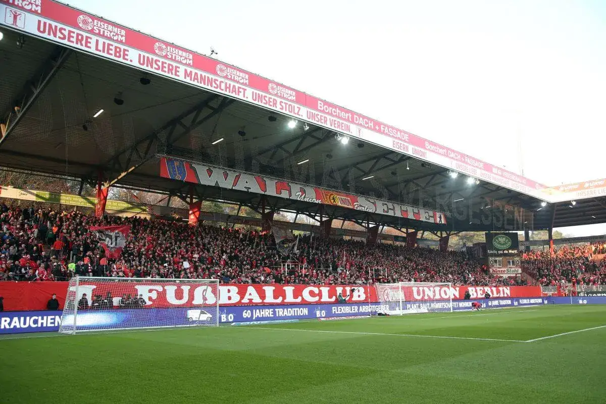 Trybuna pełna kibiców na stadionie Union Berlin. Na czerwonym banerze widnieje napis