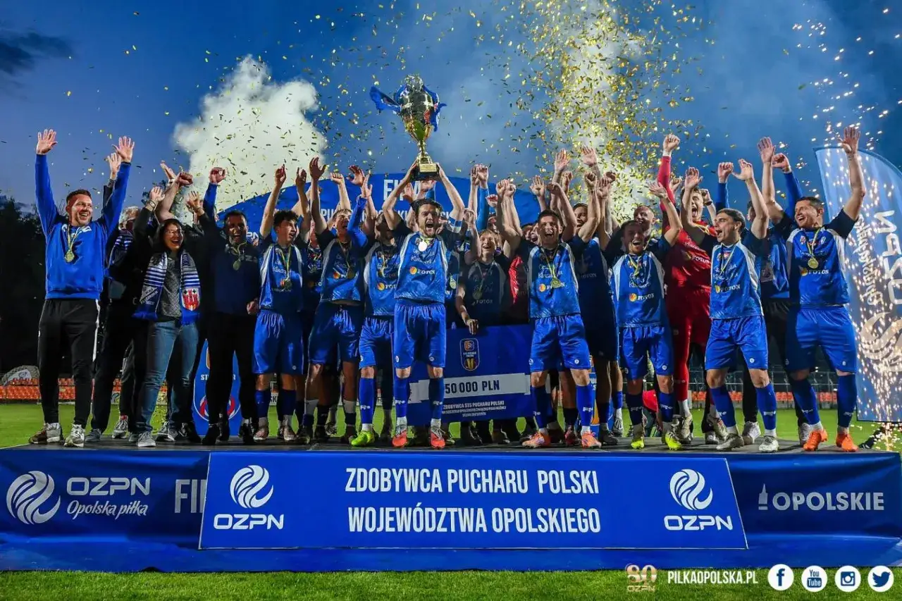 Drużyna świętuje zdobycie regionalnego pucharu polski, wznosząc trofeum i obsypana złotym konfetti.