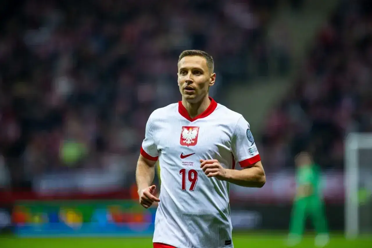 Piłkarz Przemysław Frankowski w białej koszulce z numerem 19, reprezentujący Polskę. Jego obecne drużyny to RC Lens i reprezentacja Polski.