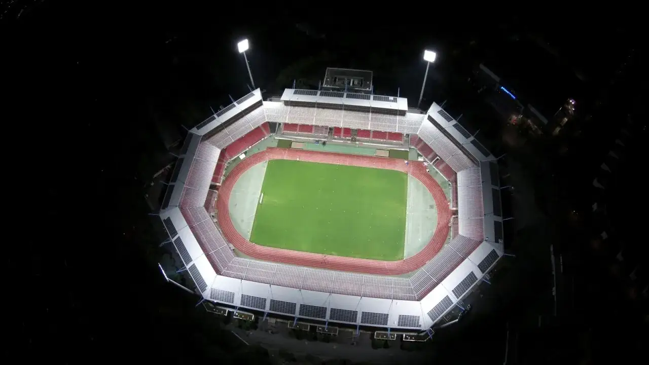 Nocne zdjęcie z lotu ptaka na oświetlony Max Morlock Stadion. Zielona murawa i bieżnia otoczone trybunami.