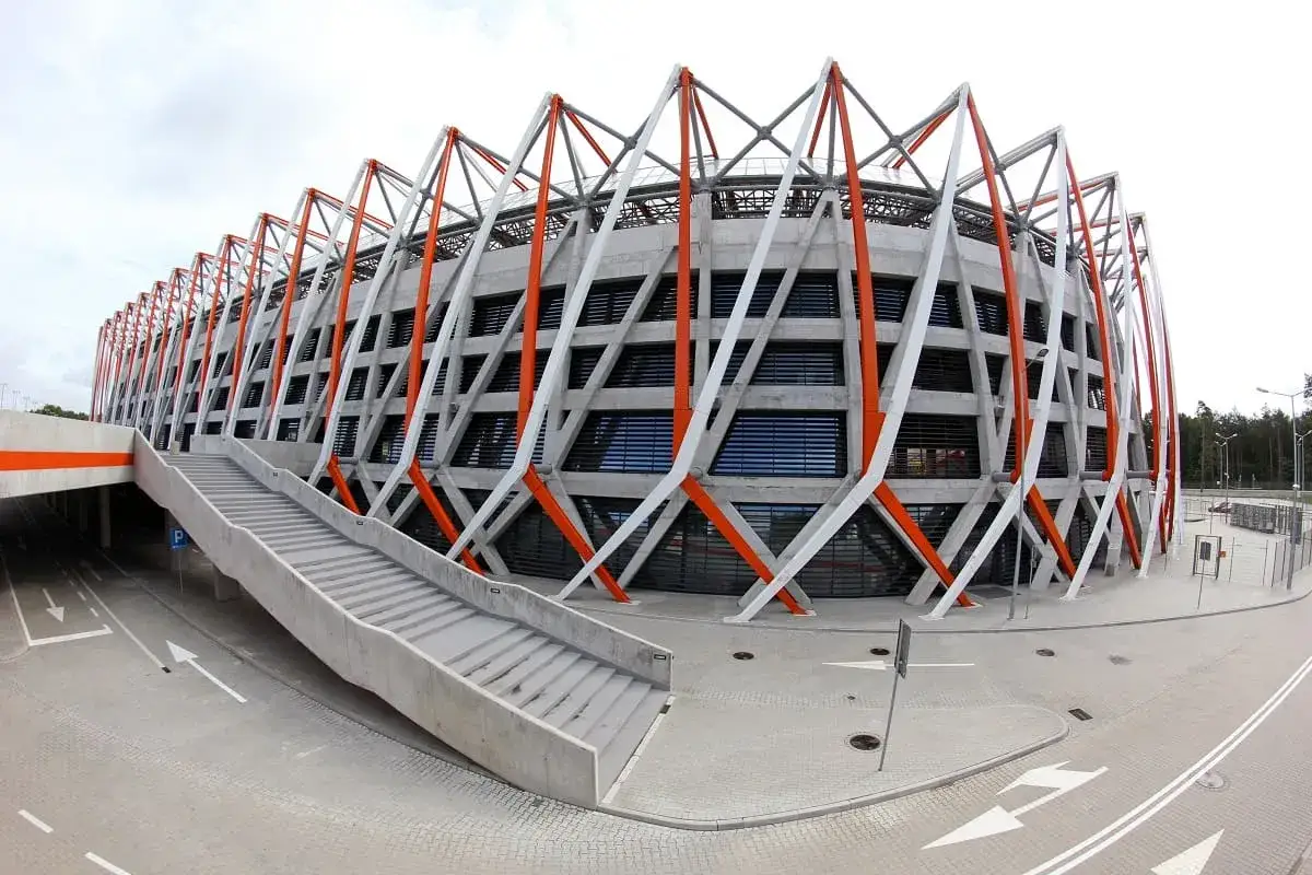 Nowoczesna architektura stadionu Chorten Arena Białystok z charakterystycznymi, ukośnymi elementami elewacji w kolorach białym i pomarańczowym.