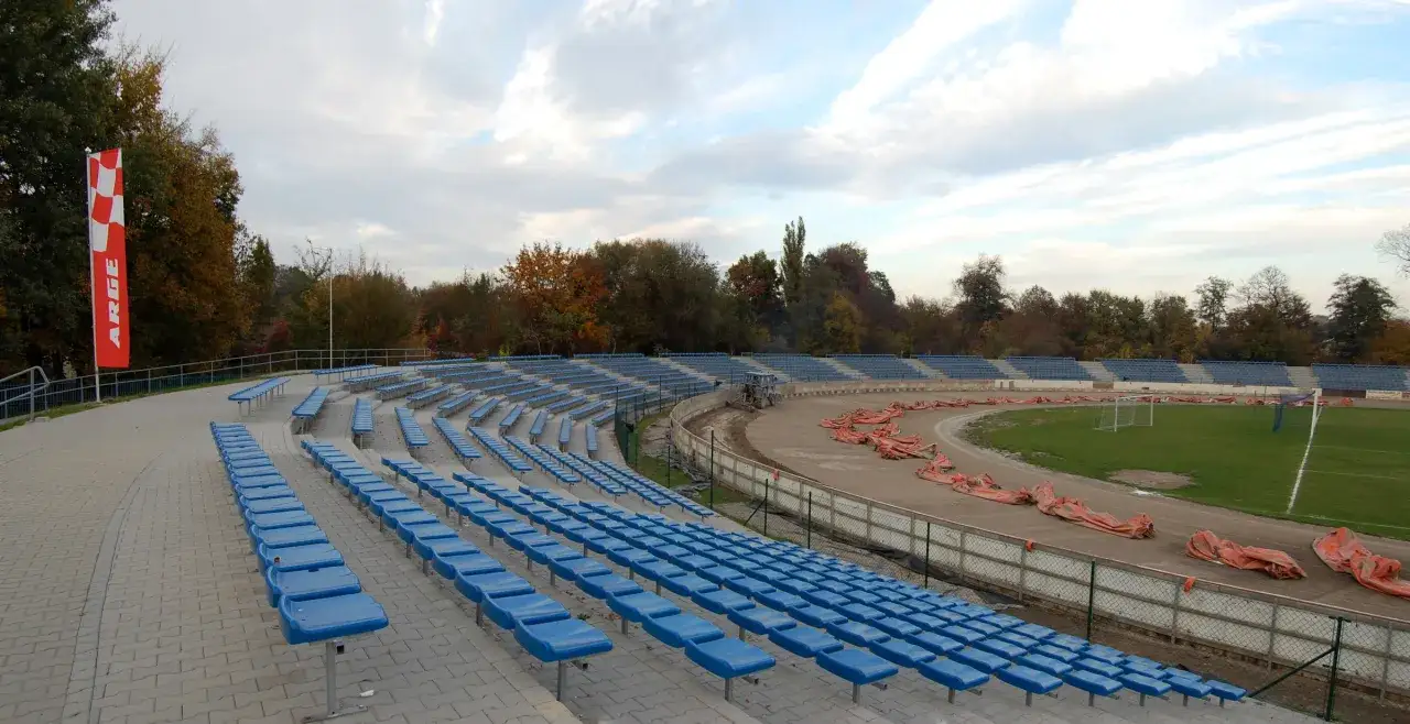 Puste trybuny stadionu Wandy Kraków czekają na kibiców. Na torze widać pomarańczowe płachty.