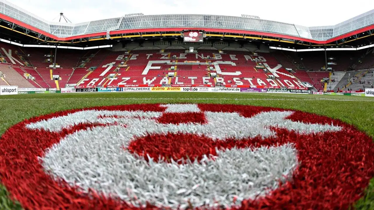 Na murawie stadionu Fritz-Walter-Stadion, symbol klubu FC Kaiserslautern. Czerwono-białe barwy drużyny dominują na trybunach i boisku.