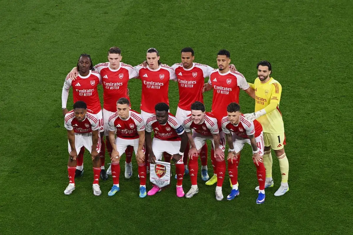 Arsenal F.C. – zawodnicy w czerwonych strojach pozują do zdjęcia na zielonej murawie. Jeden z nich trzyma transparent z logo klubu.