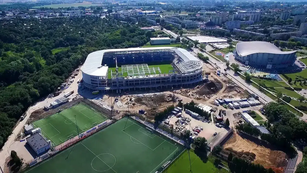 Stadion Wisły Płock w budowie, z boiskami treningowymi i otaczającą zielenią.
