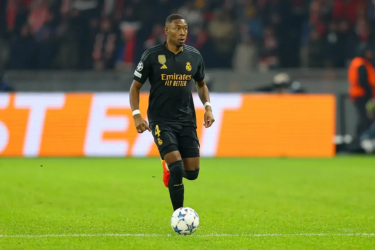 David Alaba w czarnej koszulce Realu Madryt biegnie z piłką po zielonej murawie stadionu.
