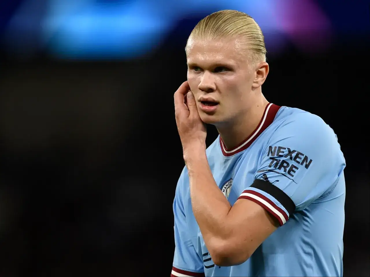 Erling Haaland, w jasnoniebieskiej koszulce z logo Manchesteru City, z dłonią przy uchu, słucha dopingu kibiców. To właśnie tam gra Haaland.