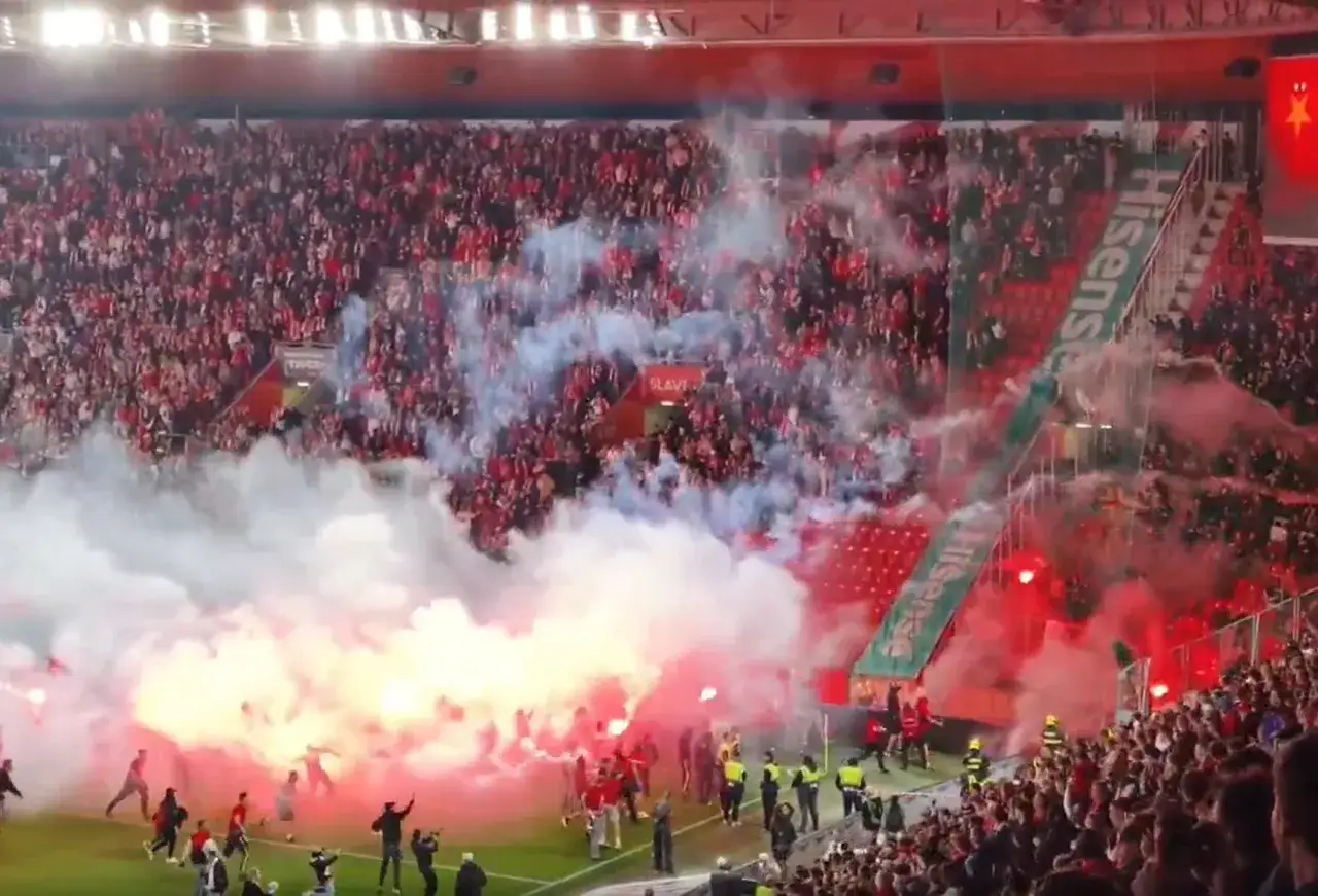 Tłumy kibiców SK Slavia Praga świętują, odpalając race i tworząc dym na boisku.