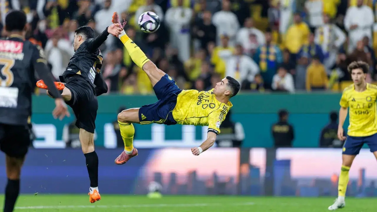 Piłkarz w żółtej koszulce wykonuje przewrotkę, gdzie gra Cristiano Ronaldo. Widownia na trybunach.
