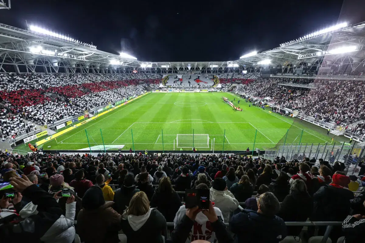 Trybuna stadionu ŁKS Ł&oacute;dź wypełniona kibicami w biało-czerwonych barwach. Piłkarze na murawie, nocny mecz.