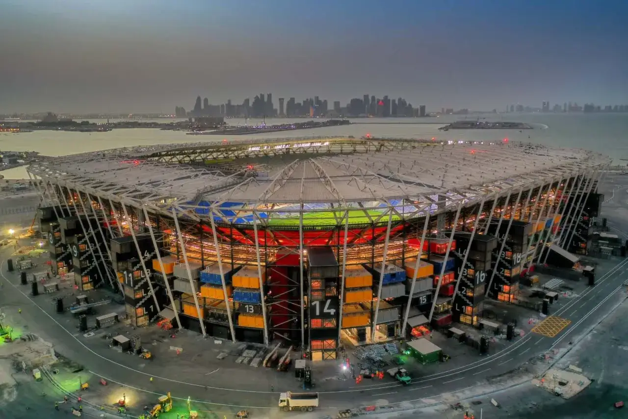 Stadion z kontenerów w Katarze, z widokiem na panoramę miasta w oddali. Konstrukcja z kolorowych modułów tworzy unikalny, nowoczesny wygląd.