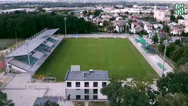 Stadion Wisłoki Dębica z zieloną murawą i trybunami, otoczony drzewami i zabudowaniami miejskimi.